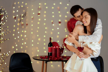 Wall Mural - Young couple with glass of wine hugging at home on Valentine's Day