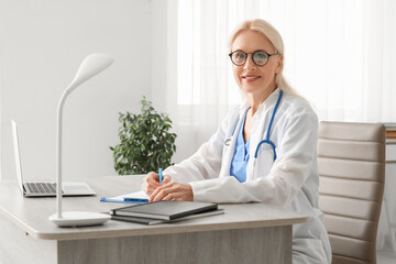 Sticker - Mature female doctor writing on clipboard at table in clinic