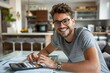 © Yuliia - The beautiful young man is smiling and wearing glasses as he diligently calculates his finance expenses at home.