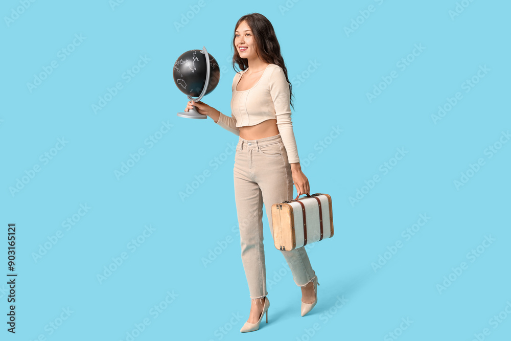 Young Asian woman with globe and suitcase on blue background. Travel concept