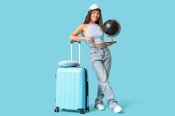 Poster - Young Asian woman with globe, suitcase and neck pillow on blue background. Travel concept