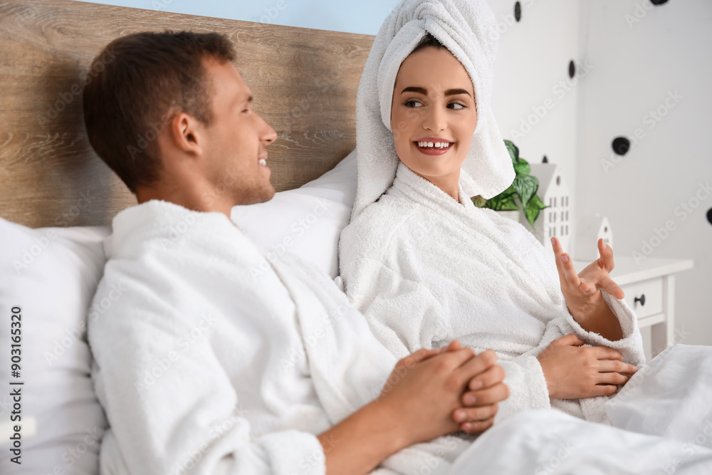 Young couple in bathrobes after shower talking on bed at home