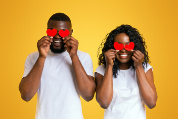 Wall Mural - African american couple closing eyes with red valentine cards, yellow studio background