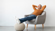 © Prostock-studio - Smiling calm mature man relaxing sitting on armchair, resting feet on knitted pouf, free copy space. Happy adult spending weekend, leaning back holding hands behind head, isolated on white studio wall
