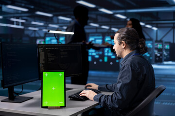 Poster - programmer works on green screen tablet in data center housing storage equipment. it professional us