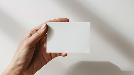 A hand holding a blank business card against a softly lit background, ideal for branding and design purposes.