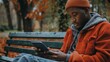 © Prostock-studio - A young man relaxes on a bench in an autumn park, focused on his tablet amid colorful fall foliage.