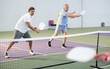 © JackF - Portrait of sporty adult man playing doubles pickleball with experienced aged partner on indoor court, ready to hit ball. Sport and active lifestyle concept