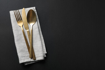 Wall Mural - Elegant golden cutlery and napkin on black background, top view. Space for text