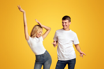 Time for fun. Happy young couple dancing together over yellow background in studio