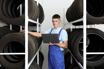 Wall Mural - Young man with laptop near car tires in auto store