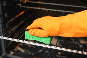 Poster - Woman cleaning oven rack with sponge, closeup