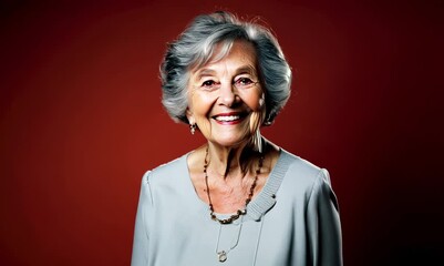 Wall Mural - Portrait of smiling senior woman with grey hair standing against red background