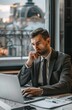 © Koja - A man in formal business attire uses a laptop in a professional setting, with large windows offering a scenic view, symbolizing productivity and modern work environments.