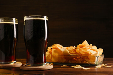 Glasses of beer and potato chips on wooden table