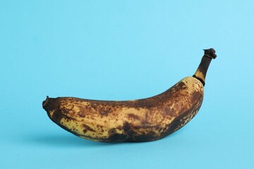 Overripe banana with dark spots on light blue background, closeup