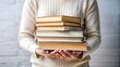 © Sniezka - Person carrying stack of books, casual wear, striped sweater, white background, pastel colors, perfect for educational websites and book club ads.