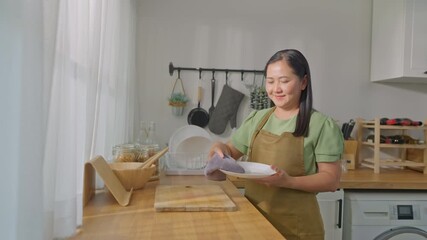 Sticker - Asian mature woman housekeeper cleaning dishes in kitchen room at home. 