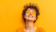 © Steven - Young woman with curly hair and sunglasses smiling against a vibrant yellow background, exuding happiness and positivity.