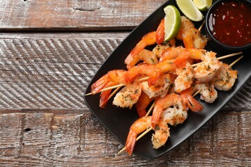 Wall Mural - Delicious grilled shrimp skewers served with sauce and lime on wooden table, top view. Space for text