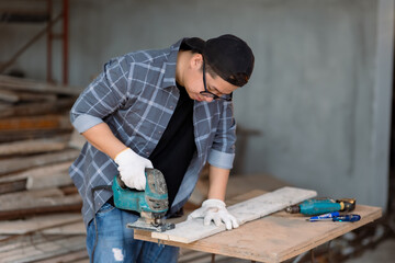 Wall Mural - Carpenter asian man cutting wooden with handsaw at under construction home.