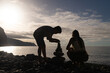 © Milou Dirks - silhouttes of boy and girl playing at the beach during sunset making tower from pebbles