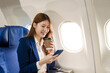 © NanSan - An Asian businesswoman takes a plane ride near the window to study abroad. She grabs a coffee, looks out the window, uses her mobile phone, smiles, and feels happy during the flight.
