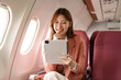 © NanSan - An Asian businesswoman takes a plane ride near the window to travel for a business discussion. She smiles while looking out the window, enjoying the journey and preparing for her meetings.