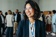 © Jacob Lund - Smiling businesswoman wearing glasses at a networking conference with colleagues in the background