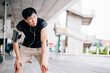 © twinsterphoto - Tired Asian guy in headphones leaning on knees and looking away while listening to music and relaxing during outdoor workout on city street
