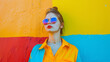 © VK Studio - A young woman wearing colorful sunglasses and a bold outfit, confidently leaning against a vividly painted wall in an urban setting.