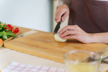 Closeup hands of asian women cutting boil egg with knife on cutting board and slice fresh vegetables to preparing ingredients for cooking breakfast meal while making healthy food lifestyle in kitchen