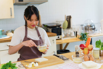 Asian women mixing mayonnaise and chopped boiled eggs for sandwich and dressing for vegetable salad while preparing ingredients for cooking breakfast meal and making healthy food lifestyle in kitchen