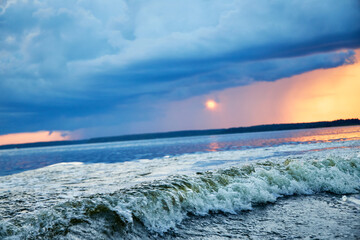 Wall Mural - A view of the wave from the boat on the river and the pink and orange sky at sunset with clouds with the reflection of the sun in the river 