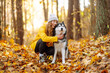 © maxbelchenko - Portrait of a curly young woman hugging her dog in the autumn park. Husky dog. Friendship, pet and human.