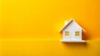 © DigitalArt Max - Vibrant yellow background features a small white toy house, symbolizing a dream home, with a blank banner above, perfect for adding mortgage or property insurance text.