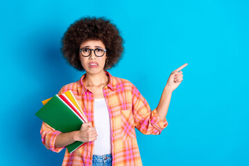 Canvas Print - Photo of attractive young girl hold copybooks nervous point empty space dressed stylish checkered clothes isolated on blue color background