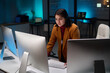© Mediaphotos - Portrait of female cybersecurity expert using computer with multiple monitors in office lit by blue light