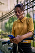 © kerkezz - Beautiful young woman pushing a bicycle walking in the park and looking at the phone.