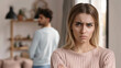 © MAHIJO - Young woman with angry expression. She is blonde with long hair, wearing a soft pink sweater. There is a dark-haired man behind her. Concept of love quarrel and disagreements in a relationship.
