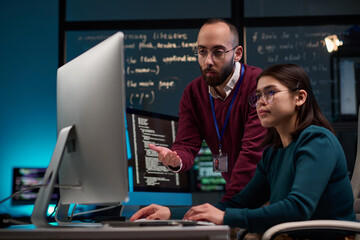 Portrait of bearded adult man as IT development supervisor advising young trainee in office and pointing at computer screen copy space