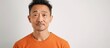 © Ilgun - An Asian man in an orange shirt with a neutral expression in a portrait against a plain white background suitable for copy space image
