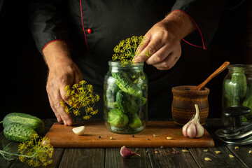 Wall Mural - The cook adds dill to a jar of cucumbers before canning. The concept of making pickled delicious cucumbers on the kitchen table by the hands of the chef