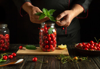 Wall Mural - A chef adds fresh mint to a jar of cherries by hand. Preparing canned compote on the kitchen table by the hands of a cook.