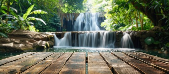 Wall Mural - A wooden table with a blurred tropical waterfall background provides copy space for product advertisements showcasing the scenic summer setting