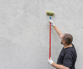 Wall Mural - A man colors a wall with a roller, showcasing concentration and effort in a well-lit room filled with anticipation for transformation.