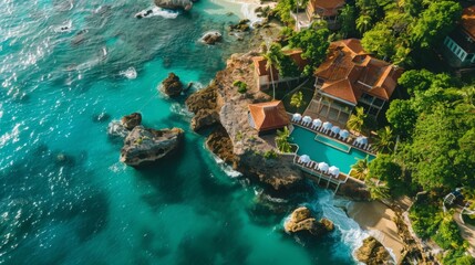 Aerial drone above view of luxury resort hotel villa building with swimming pool on sea or ocean water coast with rocks