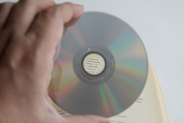 Aufkleber - A hand holding a CD against the background of an open book with text, English language learning, educational courses, self-learning