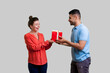 © khosrork - Portrait of loving smiling man giving wrapped present boxsurprisedwoman couple standing together expressing happiness. Indoor studio shot isolated on gray background.