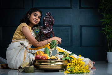 Kerala Vishu festival photography, Young Indian girl wearing traditional saree and holding Lord Krishna sculpture with Vishu kani on the background, Krishna Janmashtami image